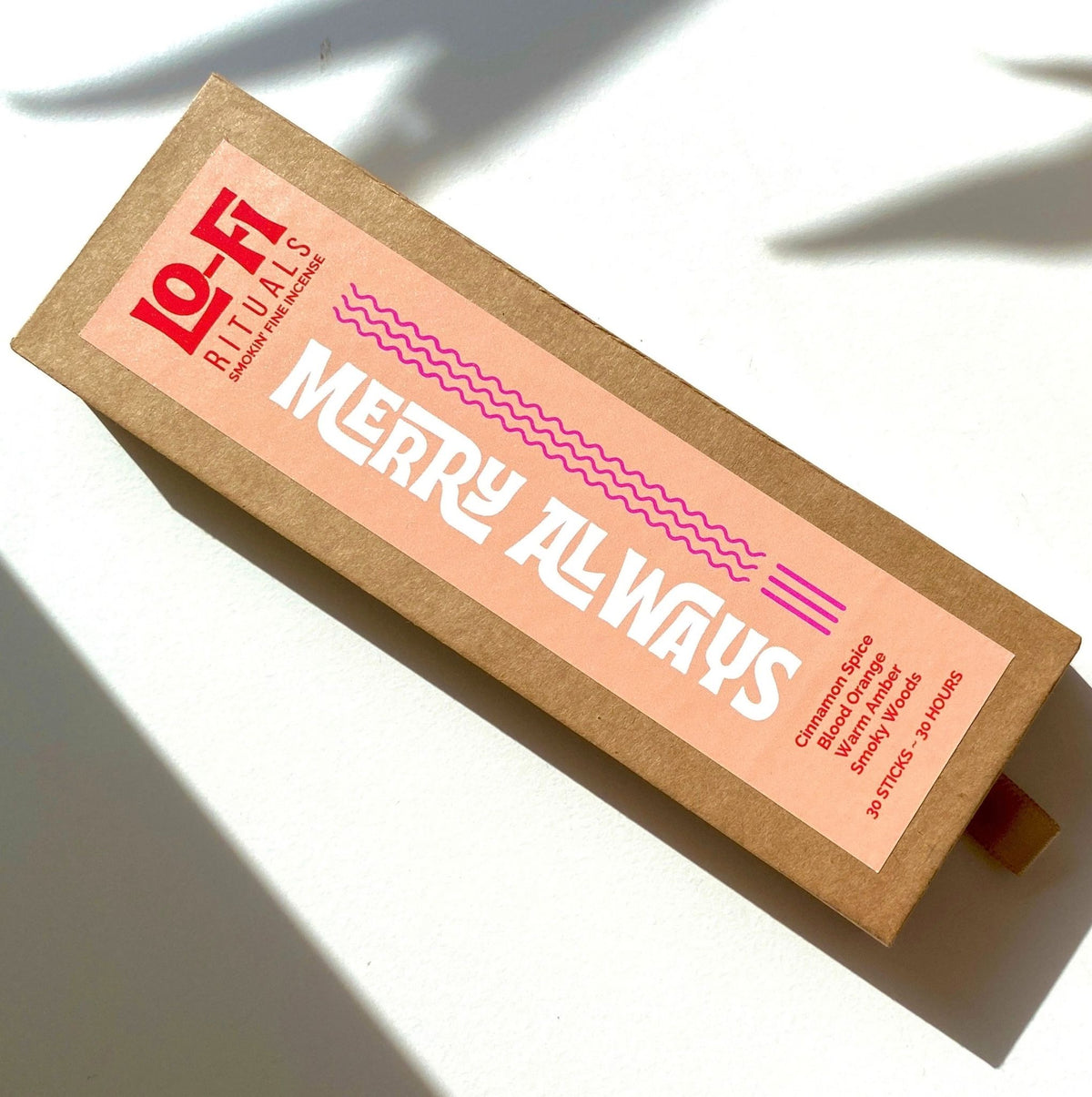 A rectangular kraft paper box of Lo-Fi Rituals incense sits on a sunlit white background, featuring a modern, bold label in eye-catching peach, red and hot pink.
