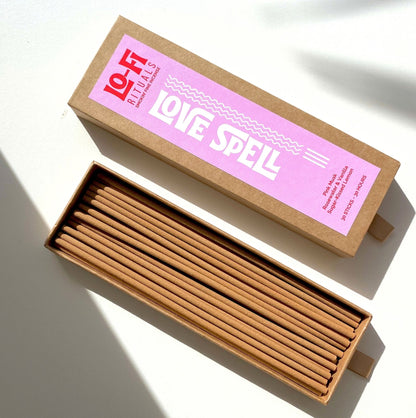 A sliding drawer box of incense sticks, shown open with the incense sticks inside and lid with colourful pink and red label above for Lo-Fi Rituals Love Spell incense 
