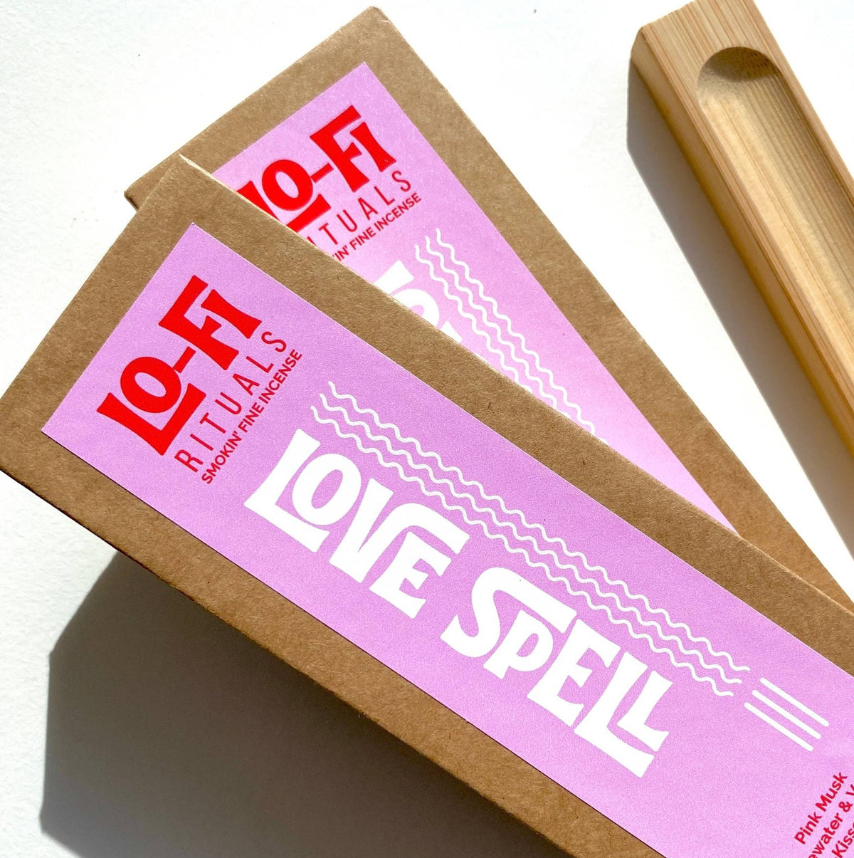 Two brown kraft paper boxes of Lo-Fi Rituals 'Love Spell' incense sticks on a white background, with a bamboo incense holder