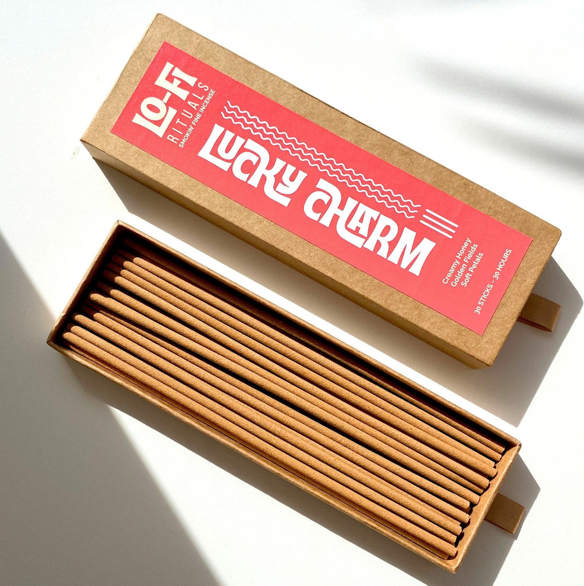 An open box of Lo-Fi Rituals Lucky Charm incense on a bright white background, the golden brown incense sticks are visible in the box