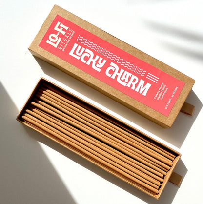An open box of Lo-Fi Rituals Lucky Charm incense on a bright white background, the golden brown incense sticks are visible in the box