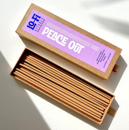 An open box of Lo-Fi Rituals Peace Out incense. The sun shines on the golden oak wood incense sticks. The modern, bold label includes scent notes for lavender, herbs, amber and vanilla.