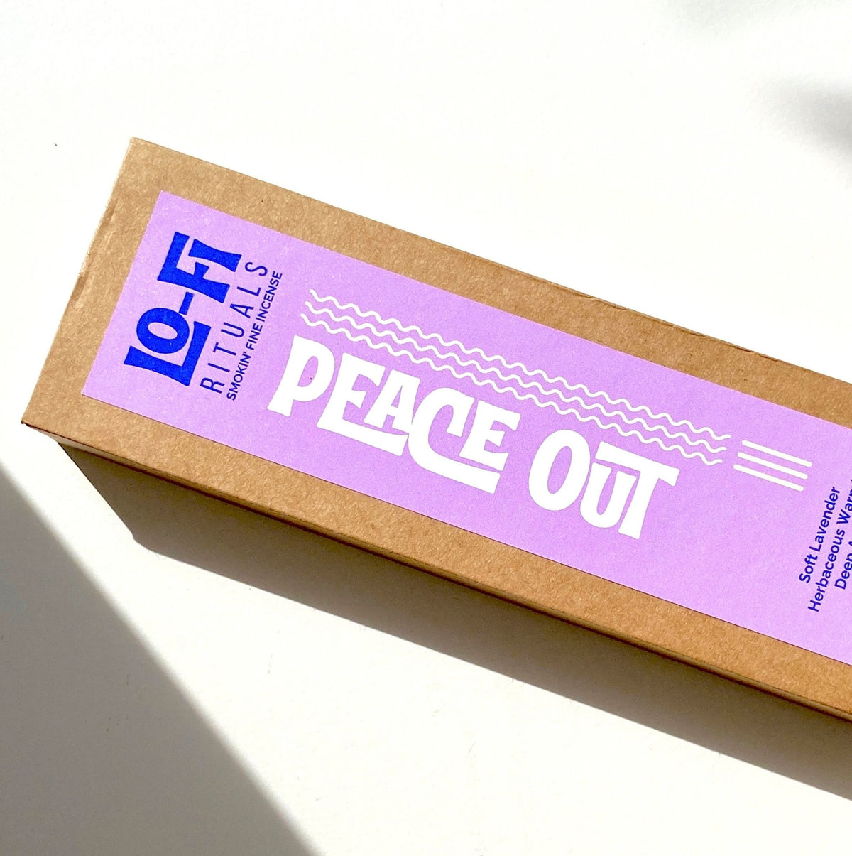 A slightly cropped image of Lo-Fi Rituals Incense, Peace Out scent. A white background with stylised shadow in the the corner. The modern, bold lilac and blue label pops with the white product name contrasting strongly.