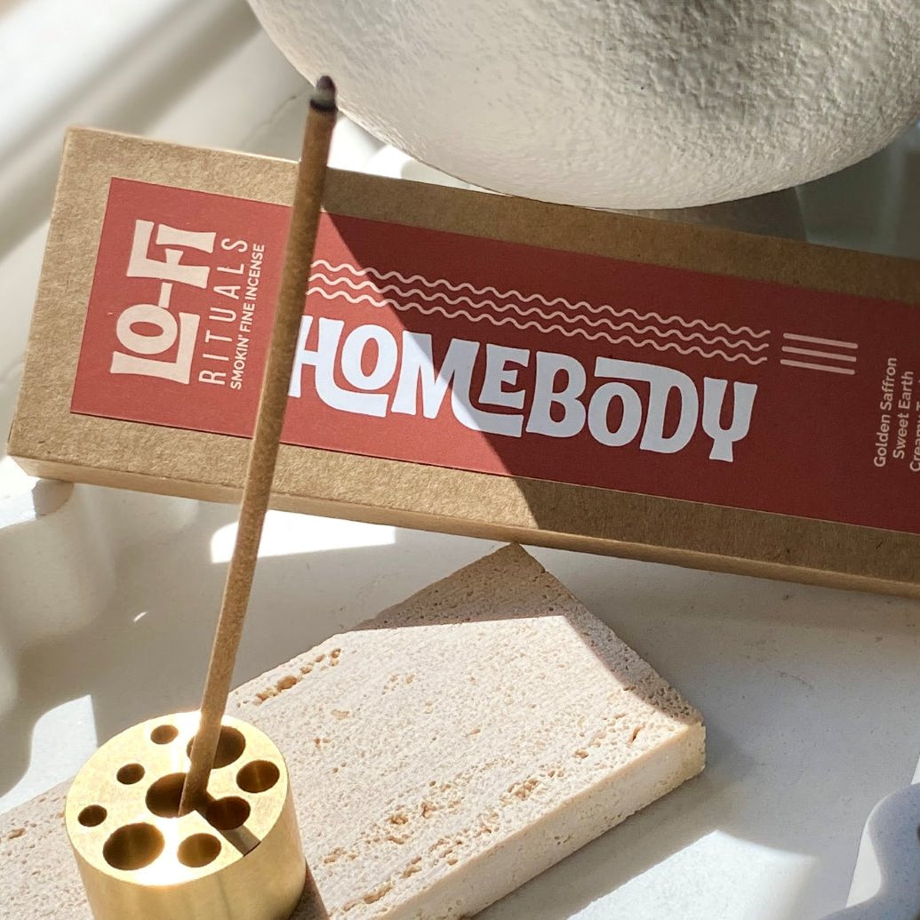 Lo-Fi Rituals Homebody incense product with natural incense stick burning in brass incense holder in sunlight on a white ceramic tray .
