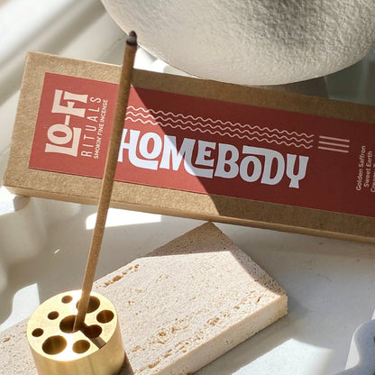 Lo-Fi Rituals Homebody incense product with natural incense stick burning in brass incense holder in sunlight on a white ceramic tray .