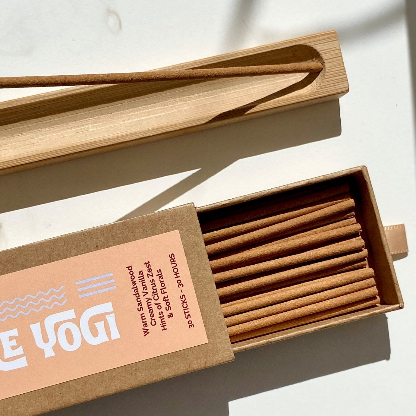 Open box of Lo-Fi Rituals Part-Time Yogi sandalwood incense sticks on a light background next to a wooden incense holder