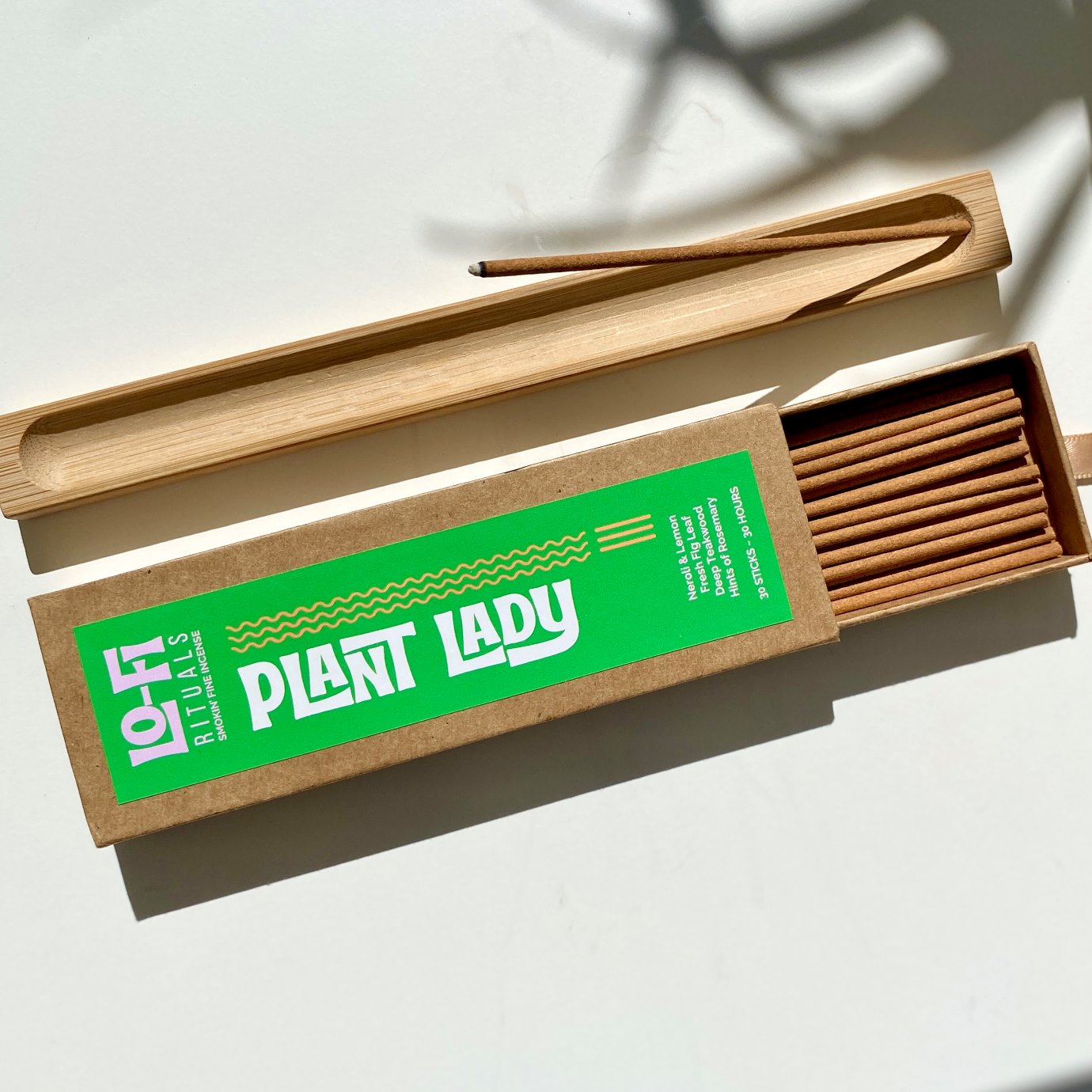 Sunlit image of Lo-Fi Rituals Plant Lady incense on a sunlit white background, next to a wooden incense holder