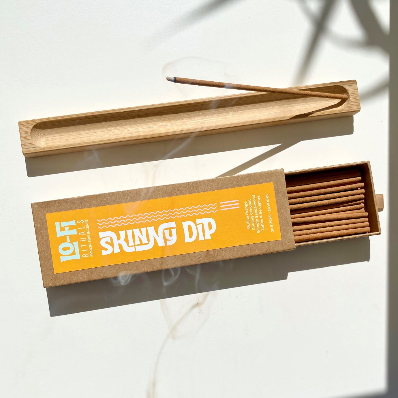 Open box Lo-Fi Rituals Skinny Dip incense next wooden incense holder burrning incense with curling smoke 