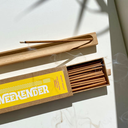 Open box of incense sticks next to wooden holder with burining incense and curling smoke