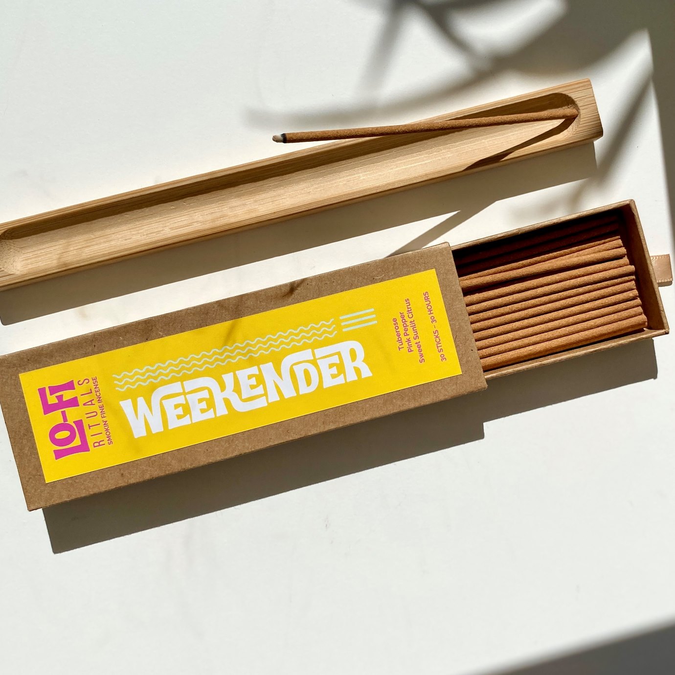 Open box of 'Lo-Fi  Rituals Weekender' incense sticks and wooden incense holder on a light background in full sun with cinematic shadows